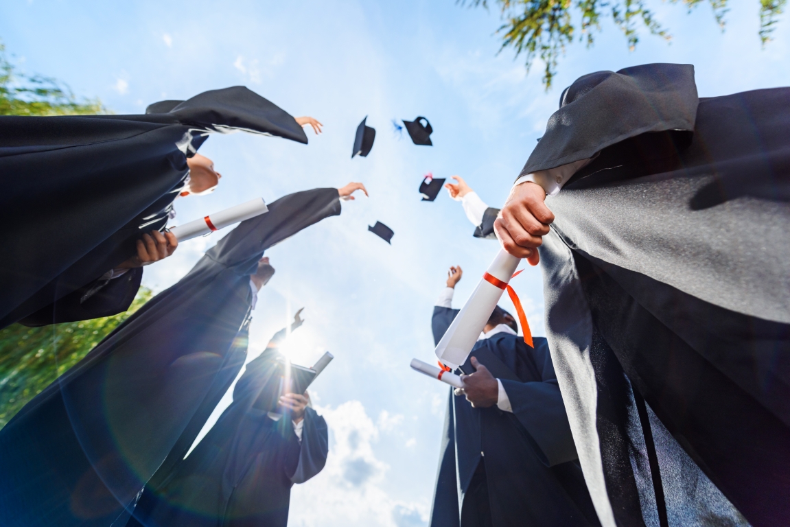 bottom view of graduated students throwing up hats in front of blue sky