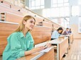 International group of people sitting at separate tables in lecture hall of modern college, focus on beautiful blonde woman s in foreground